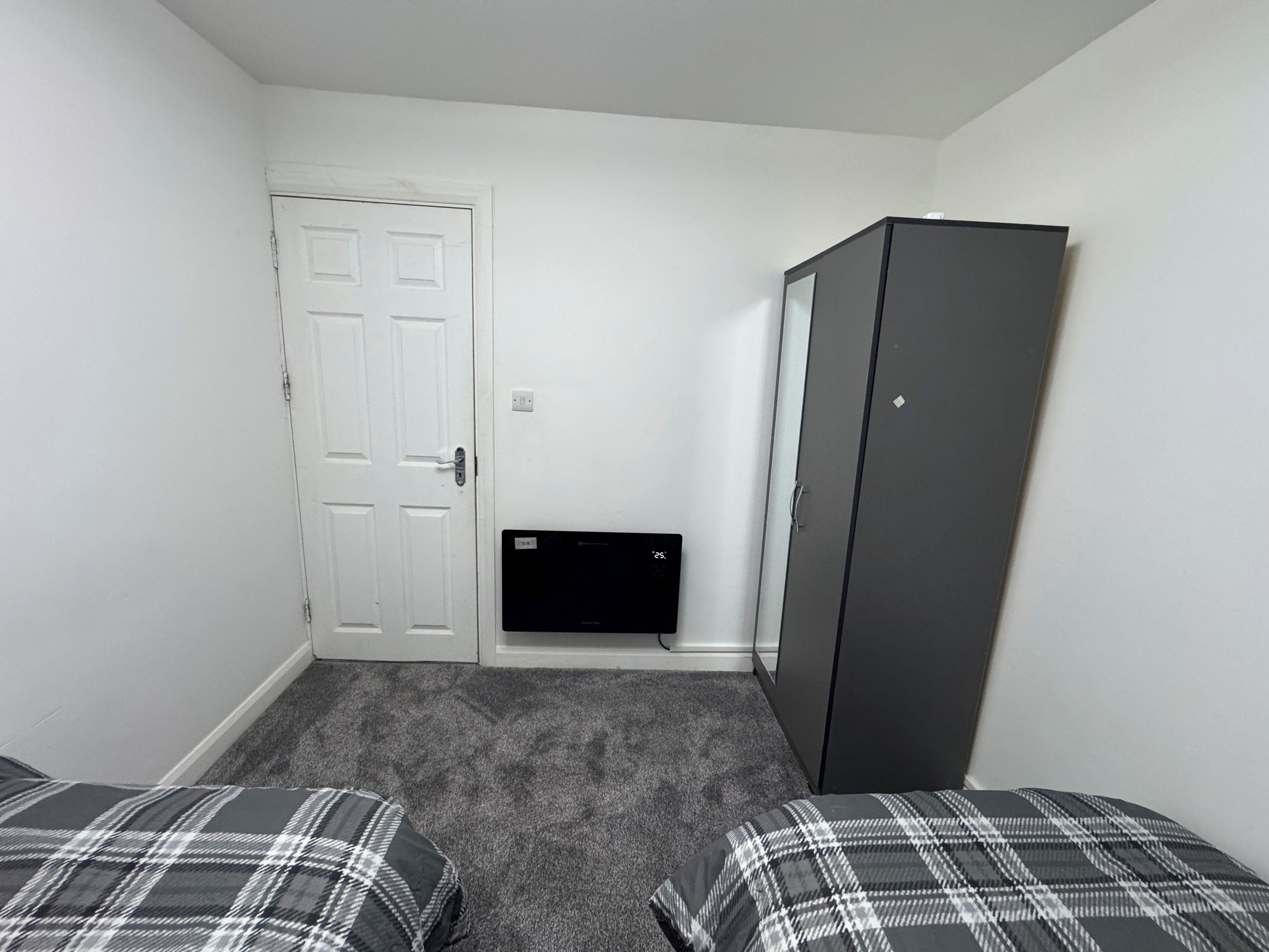 A small, sparsely furnished room with a white door, a black cabinet, and a small black device on the wall.