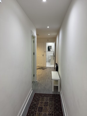 A hallway with a white door, a bench, and a patterned rug leading to a bathroom with a white toilet and a mirror.
