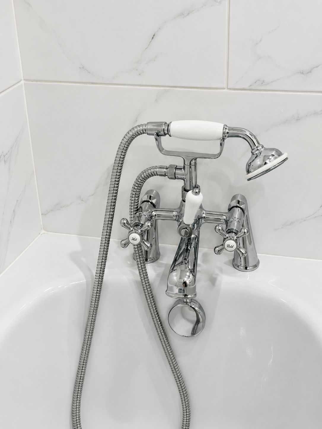 A bathroom with a chrome bathtub, a handheld showerhead, and a flexible hose.