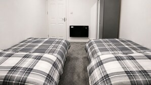 A room with two beds, a white door, a grey wardrobe, and a small plant on top. - Wimbledon Lodge (London)