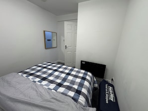 A bedroom with a checkered bedspread, a mirror, a door, and a suitcase.