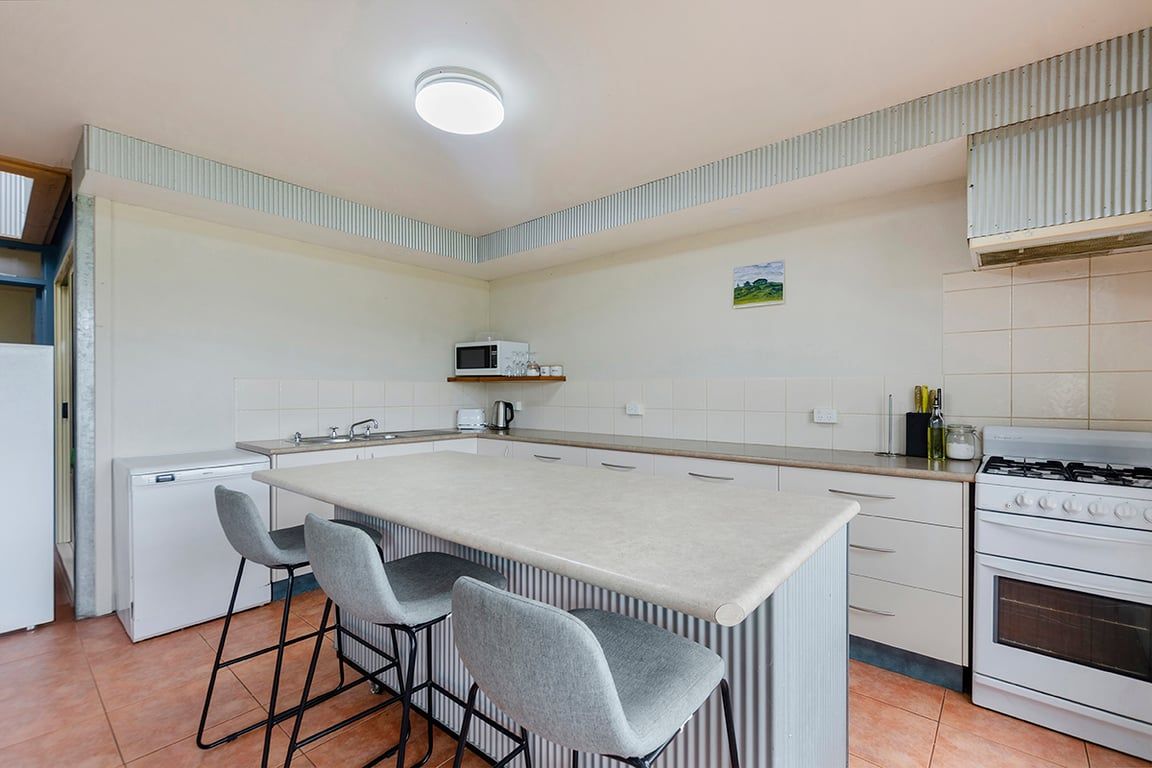 Cocina compacta con una isla central, taburetes de bar, microondas, estufa y refrigerador.
