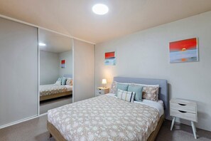 A bedroom with a bed, bedside tables, a mirror, and two wall-mounted paintings. - Eye of The Dune (Glenelg)