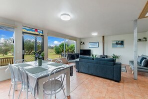 A spacious living area with a dining table, chairs, a sofa, and a TV. - Eye of The Dune (Glenelg)