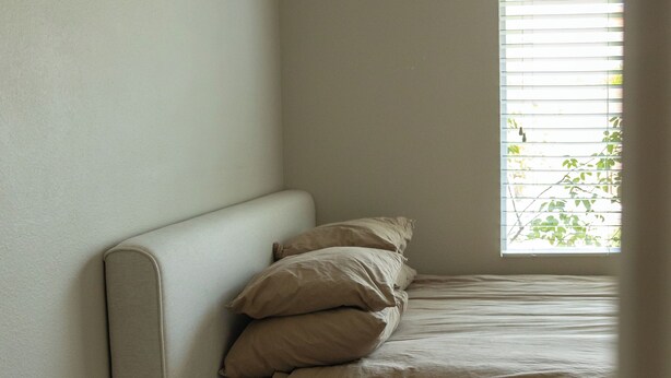 Une chambre à coucher avec un lit, des oreillers, une table de chevet et une fenêtre.