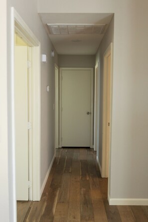 A narrow hallway with wooden flooring, white walls, and a closed door at the end. - 3-bedroom Desert Escape Near Saguaro Lake & Salt River (Mesa)