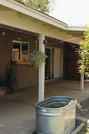 A residential building with a concrete patio, a hanging plant, a metal planter with greenery, and a window with blinds. - 3-bedroom Desert Escape Near Saguaro Lake & Salt River (Mesa)