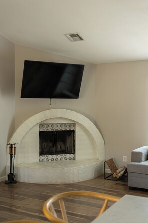 A living room with a flat-screen TV mounted above a fireplace, a sofa, and a wooden chair. - 3-bedroom Desert Escape Near Saguaro Lake & Salt River (Mesa)