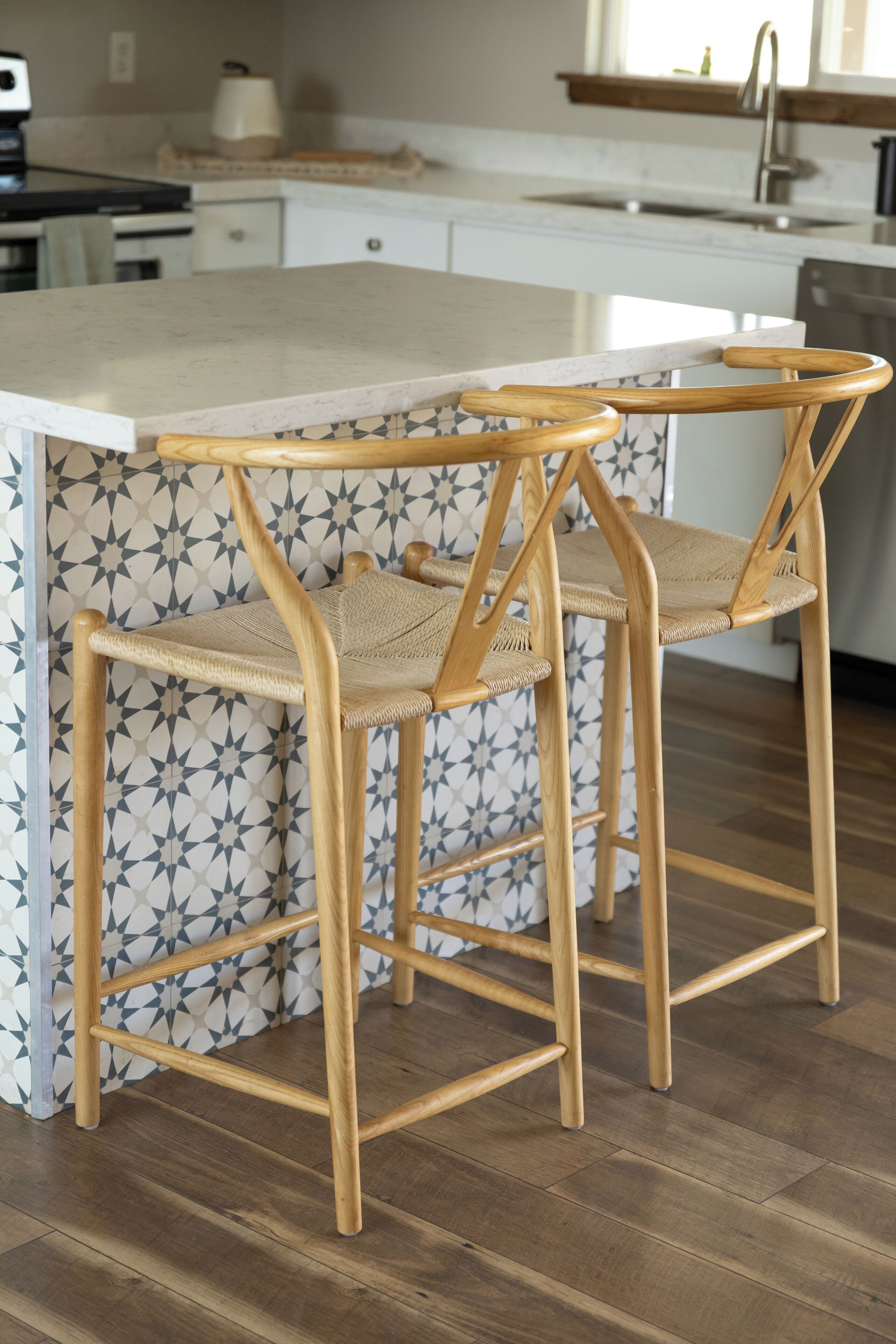 A kitchen with a white countertop, two wooden chairs with woven seats, and a patterned backsplash.