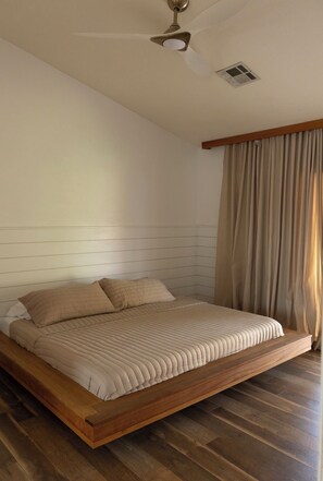 Ein Schlafzimmer mit Bett, Holzboden, Deckenventilator und einem Fenster mit Vorhängen.