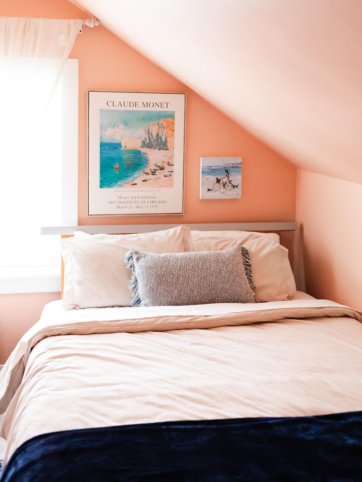 A bedroom with a bed, pillows, and a framed artwork of Claude Monet.