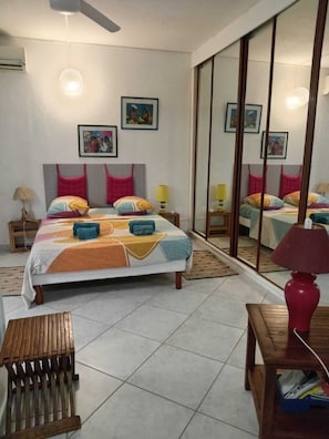 A bedroom with a bed, bedside tables, a mirror, and a wooden bench. - 2-bedroom apartment in peaceful Les Trois-Îlets with AC (Les Trois-Îlets)