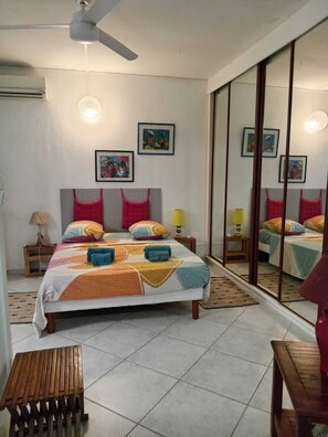 A bedroom with a bed, a bedside table, a lamp, a mirror, and a ceiling fan. - 2-bedroom apartment in peaceful Les Trois-Îlets with AC (Les Trois-Îlets)