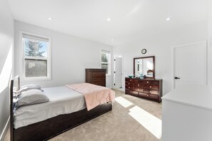 A bedroom with a bed, dresser, and a mirror. There are windows and a door. - Grand 5BR Luxury Home ! AC and Home Theater (Surrey)