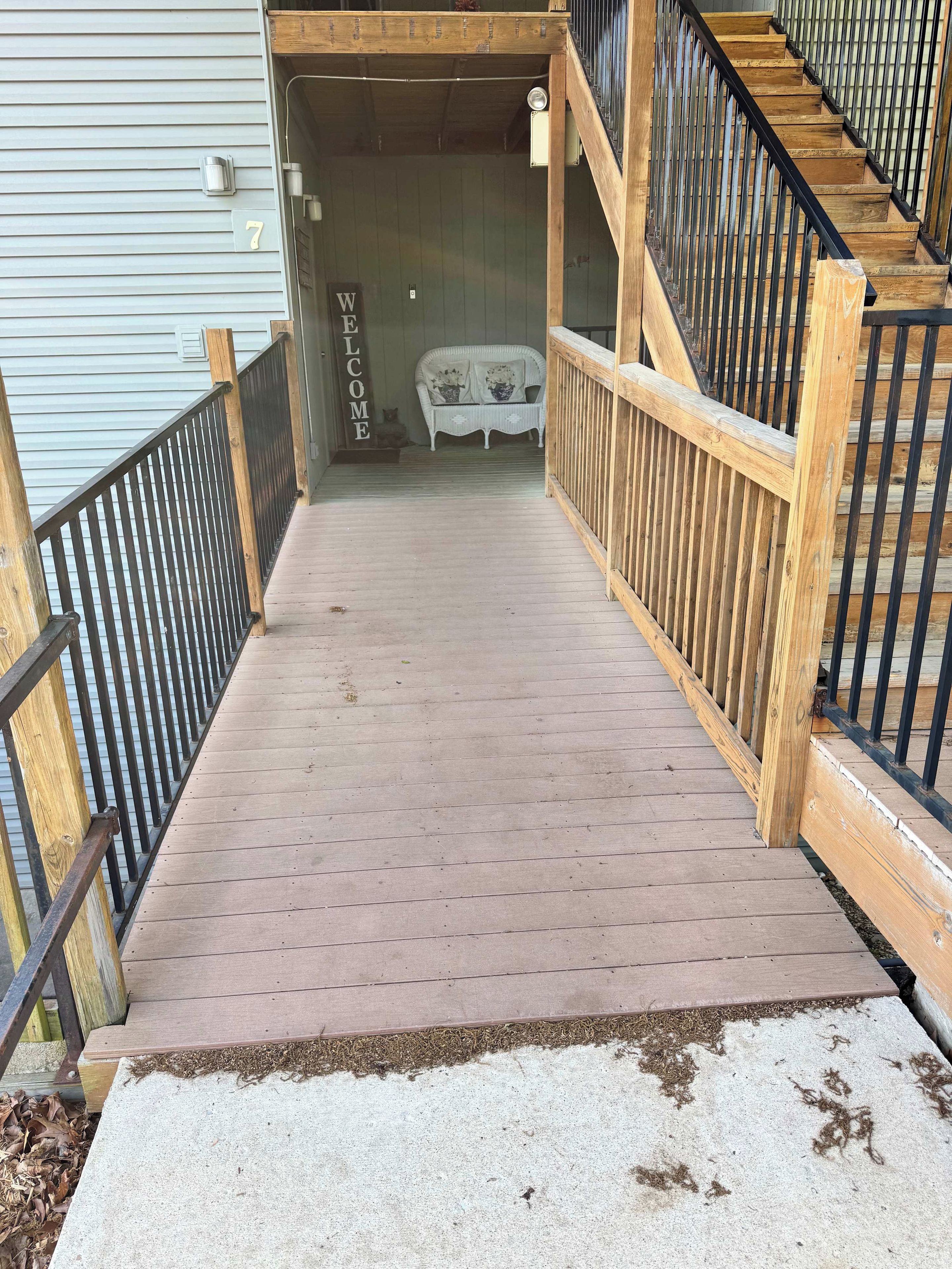 A wooden staircase leading to a porch with a 'WELCOME' sign, a white bench, and a mailbox marked with the number 7.