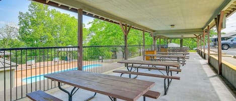 An outdoor covered picnic area with picnic tables and a pool in the background.
