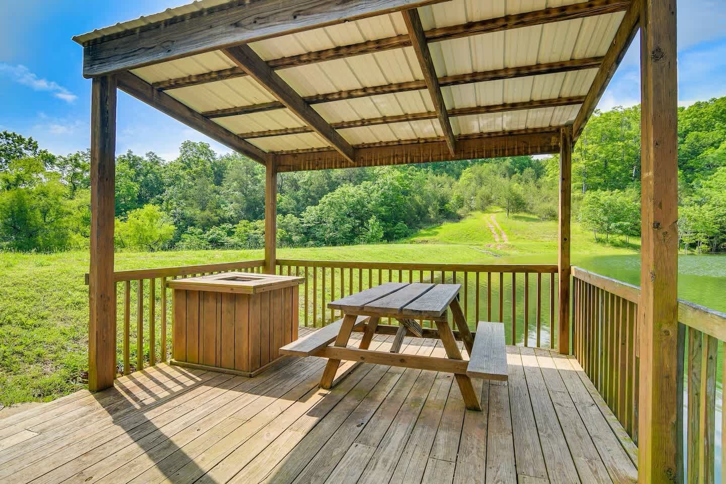 A wooden deck with a covered picnic area, a grill, and a view of a green landscape.