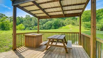 A wooden deck with a covered picnic area, a grill, and a view of a green landscape.