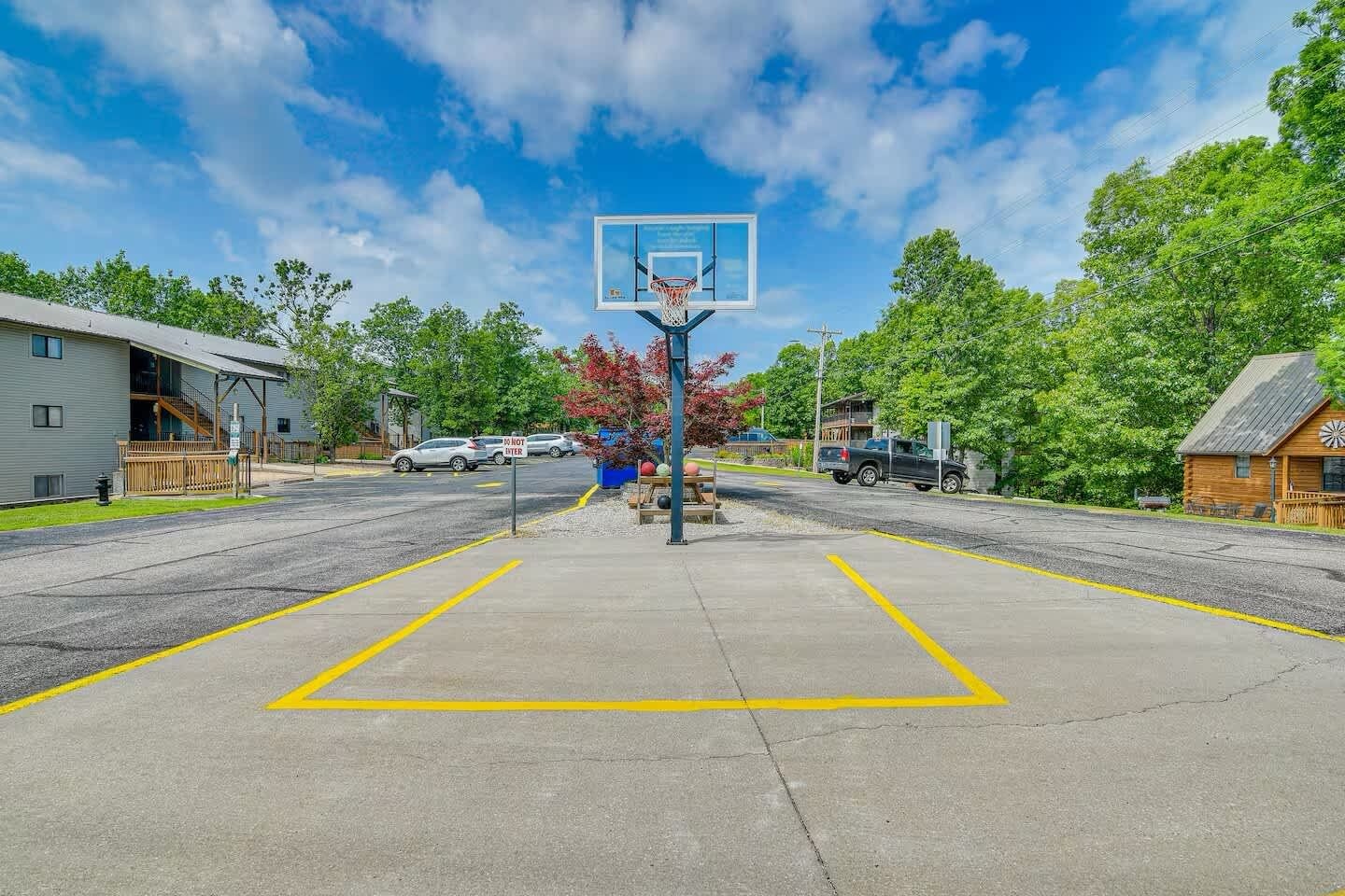 A basketball court with a hoop, surrounded by a parking lot and buildings.
