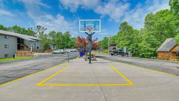 A basketball court with a hoop, surrounded by a parking lot and buildings.