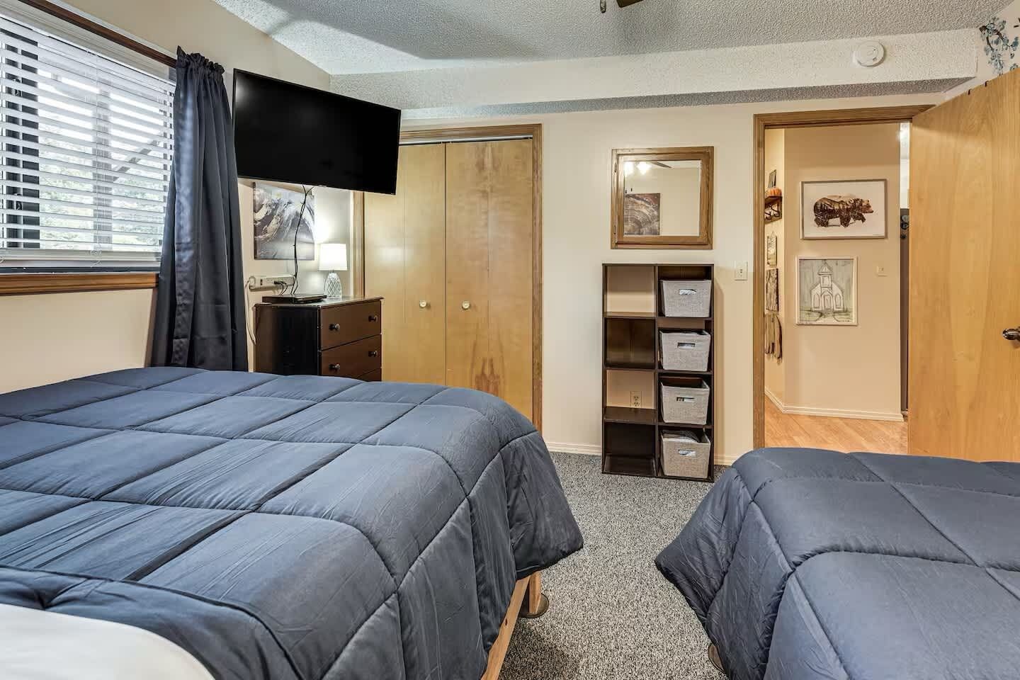A bedroom with two beds, a TV, a wardrobe, and a shelf with storage boxes.