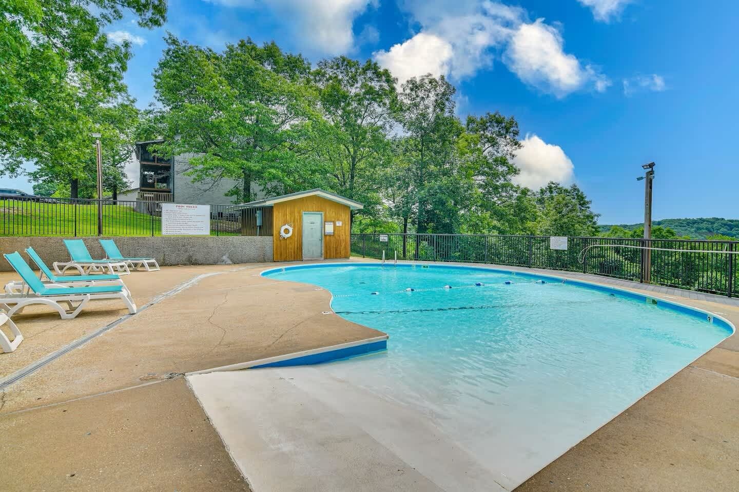 A swimming pool with lounge chairs and a small wooden building, surrounded by a fence and trees.
