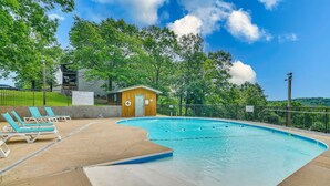 Una piscina con lettini e un piccolo edificio in legno, circondata da una recinzione e alberi.