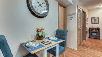 A dining area with a table set for two, a wall clock, and a decorative wall piece.