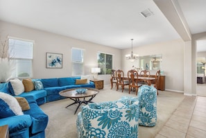 A living room with a blue sofa, a round coffee table, and a dining area with wooden chairs and a chandelier. - Welcome to Casa de Las Mariposas! Single Story, 3 Bed, 3 Bath, Fire Pit & Views! (San Marcos)