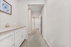 A narrow hallway with white walls, a beige carpet, and a door at the end. - Welcome to Casa de Las Mariposas! Single Story, 3 Bed, 3 Bath, Fire Pit & Views! (San Marcos)
