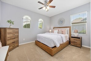 Une chambre à coucher comprenant un lit, une commode, des tables de chevet et un ventilateur de plafond.