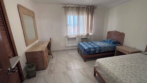A bedroom with a bed, a desk, a chair, a mirror, and a window with curtains. - For rent in one of Manzanillo's most well-equipped and sought-after condominium complexes. (Manzanillo)