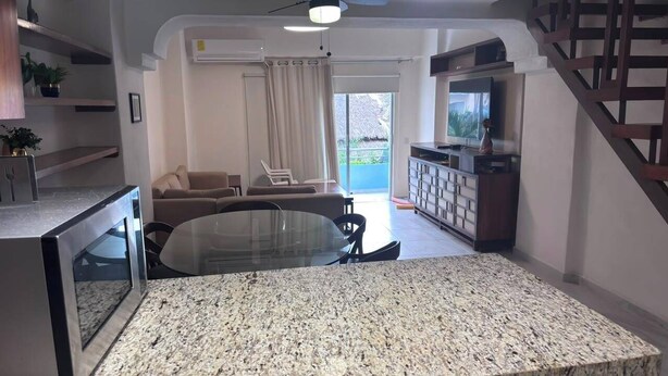 A modern living room with a glass-top dining table, a sofa, and a TV. - For rent in one of Manzanillo's most well-equipped and sought-after condominium complexes. (Manzanillo)
