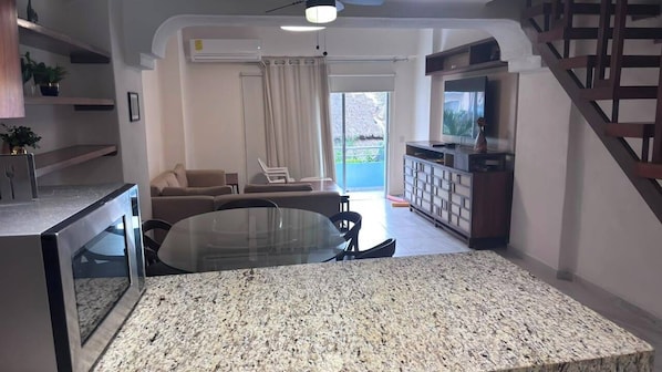 A modern living room with a glass-top dining table, a sofa, and a TV. - For rent in one of Manzanillo's most well-equipped and sought-after condominium complexes. (Manzanillo)