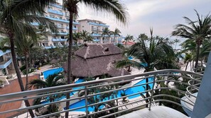 Ett semesterparadis med en pool, en byggnad med halmtak och palmer.