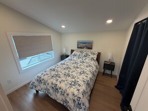 A bedroom with a bed, two bedside tables, a window with a view, and a painting on the wall. - BirdsNest 1 bedroom apartment overlooking park in Denver (Denver)