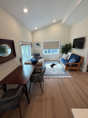 A living room with a sofa, a dining table, and a TV mounted on the wall. - BirdsNest 1 bedroom apartment overlooking park in Denver (Denver)