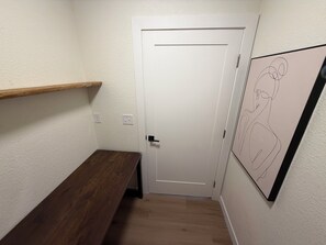 Un pasillo con un banco de madera, una puerta blanca y una obra enmarcada en la pared.