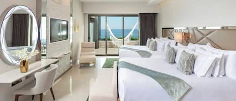 A modern hotel room with a large bed, a desk, a chair, a television, and a view of the sea.
