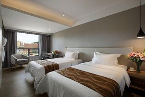 A hotel room with two beds, a desk, a chair, and a view of the city. - (Shenzhen)