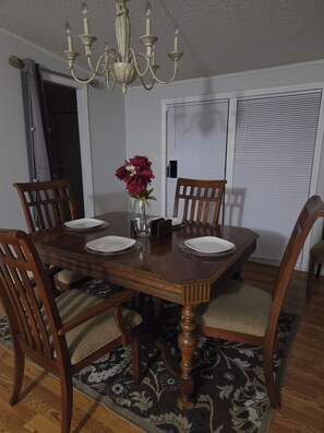 A dining room with a wooden table, four chairs, a chandelier, and a vase with flowers. - Cozy 3 bedroom house in beautiful Raeford with AC and an office. (Raeford)