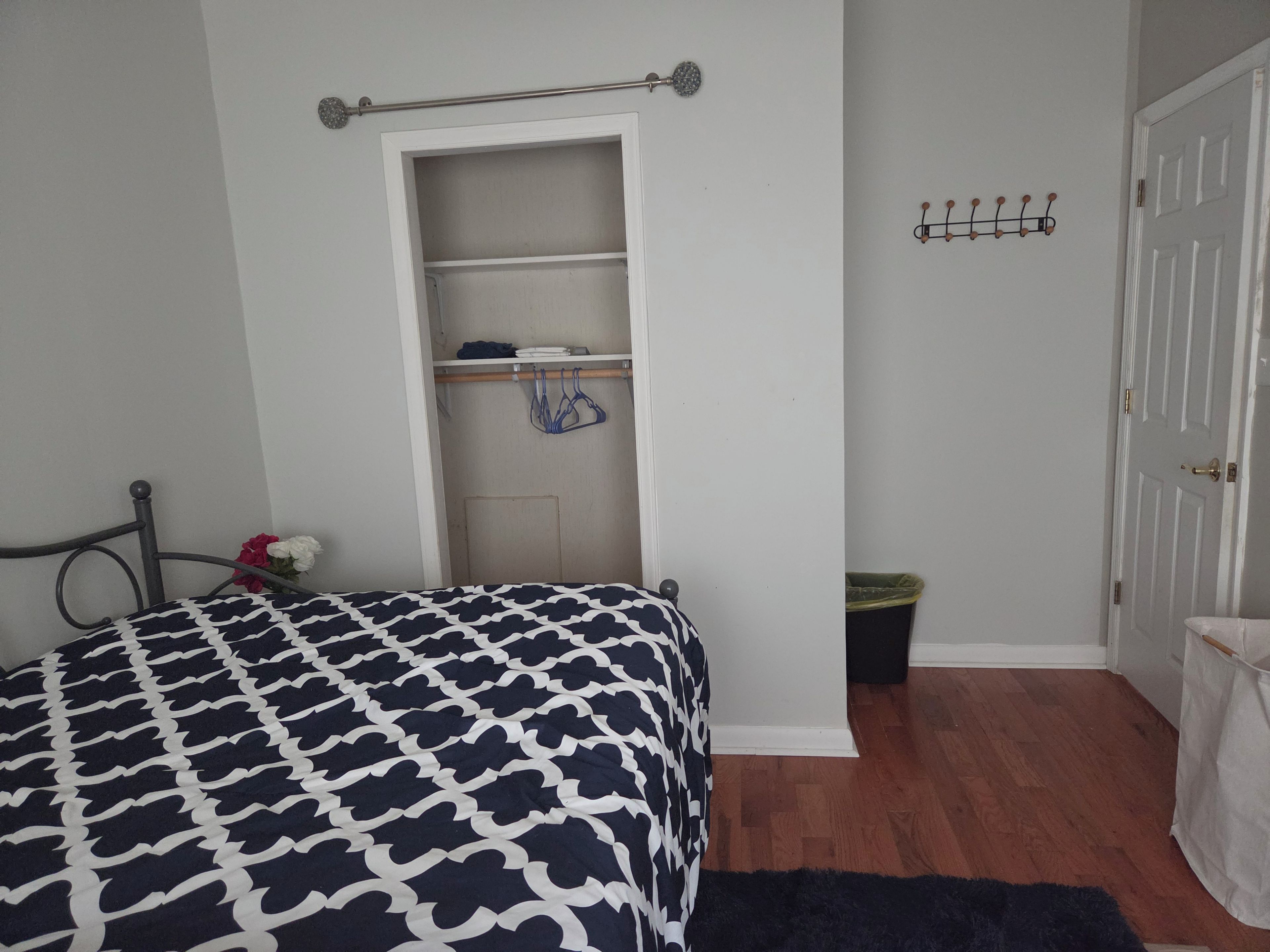 A bedroom with a bed, a wardrobe, a coat rack, and a door.