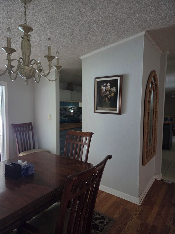 A dining area with a wooden table and chairs, a chandelier, a framed picture on the wall, and a kitchen in the background. - Cozy 3 bedroom house in beautiful Raeford with AC and an office. (Raeford)
