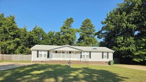 A single-story house with a front porch, a fenced yard, and a clear sky. - Cozy 3 bedroom house in beautiful Raeford with AC and an office. (Raeford)