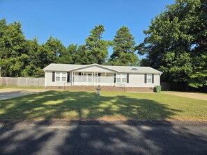 A single-story house with a front porch, a fenced yard, and a clear sky. - Cozy 3 bedroom house in beautiful Raeford with AC and an office. (Raeford)