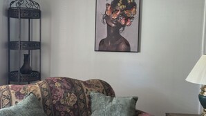 A room with a patterned sofa, a wall-mounted artwork, a decorative metal stand, and a table lamp. - Cozy 3 bedroom house in beautiful Raeford with AC and an office. (Raeford)