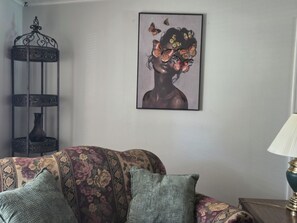 A room with a patterned sofa, a wall-mounted artwork, a decorative metal stand, and a table lamp. - Cozy 3 bedroom house in beautiful Raeford with AC and an office. (Raeford)