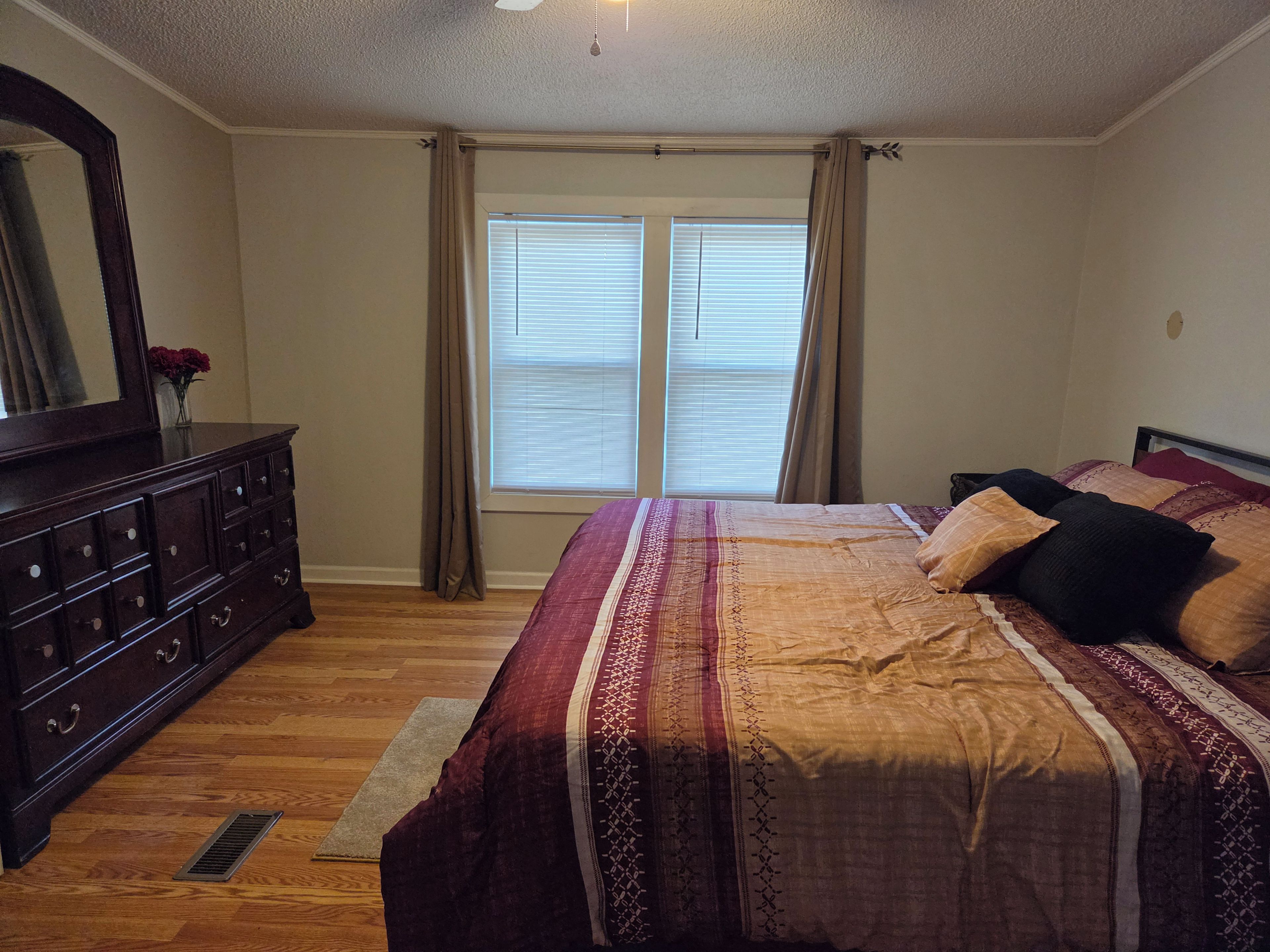 A bedroom with a large bed, a dresser, a mirror, and a window with curtains.