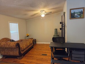 A room with a ceiling fan, a wooden floor, a sofa, a desk, and a painting on the wall. - Cozy 3 bedroom house in beautiful Raeford with AC and an office. (Raeford)