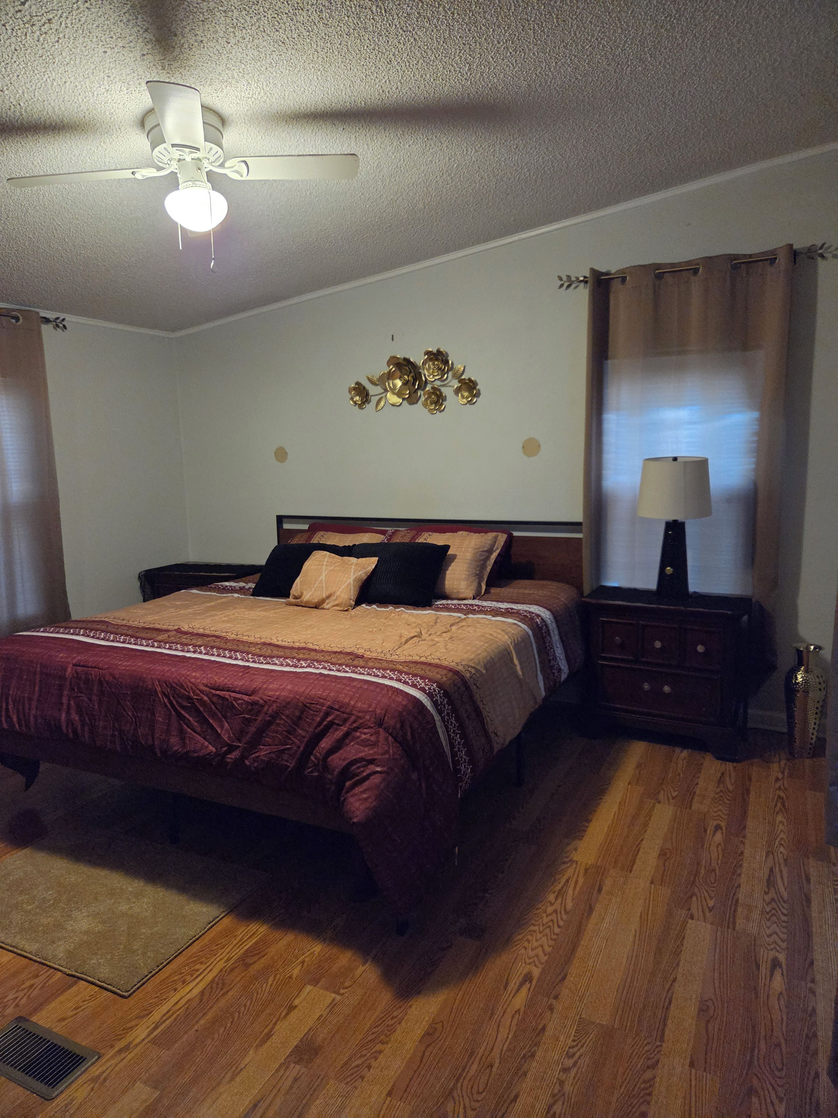Une chambre à coucher comprenant un lit, une table de chevet, une lampe, un ventilateur de plafond et un élément décoratif mural.